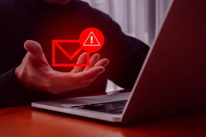 A person gestures towards a laptop, with a red email icon and an exclamation mark, indicating a warning or alert.